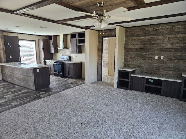 kitchen featuring gas stove, dark brown cabinets, ceiling fan, an island with sink, and wall chimney exhaust hood