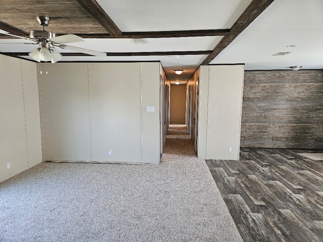 unfurnished room featuring beamed ceiling, wooden walls, a ceiling fan, and visible vents