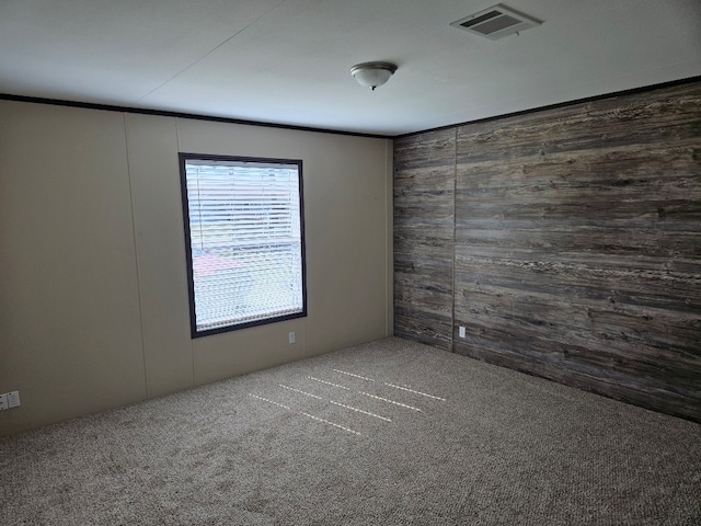 unfurnished room featuring visible vents, wood walls, and carpet floors