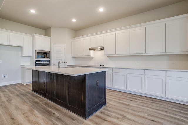 kitchen featuring light wood-type flooring, sink, black appliances, a center island with sink, and white cabinetry