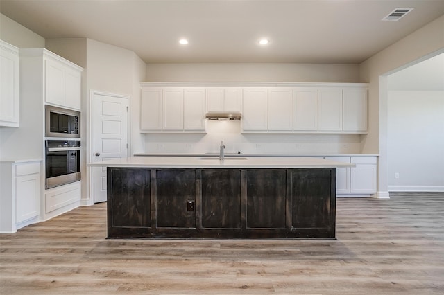 kitchen with a center island with sink, white cabinets, stainless steel appliances, and light hardwood / wood-style floors