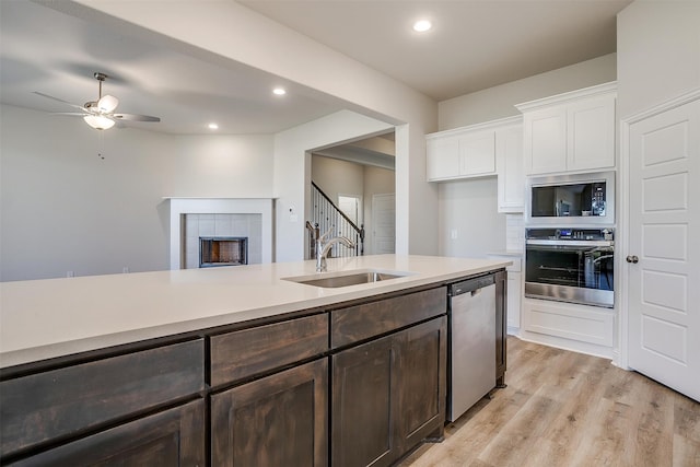 kitchen featuring a tile fireplace, white cabinetry, sink, stainless steel appliances, and light hardwood / wood-style floors