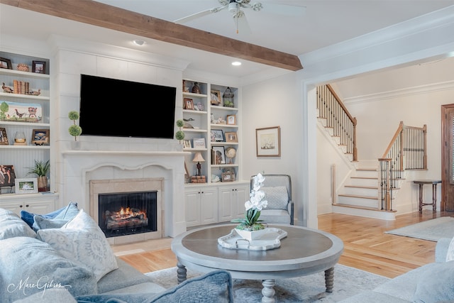 living room featuring beam ceiling, ceiling fan, built in features, light hardwood / wood-style floors, and a tiled fireplace