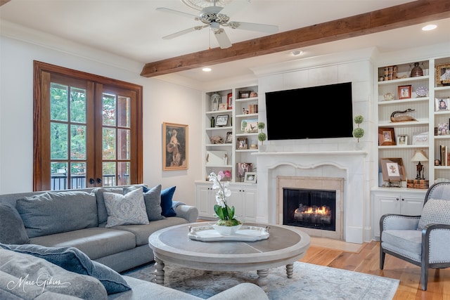 living room featuring beam ceiling, ceiling fan, french doors, light hardwood / wood-style flooring, and a tiled fireplace