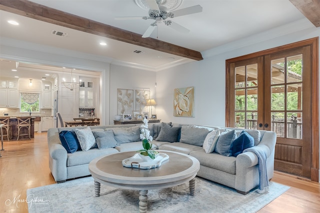 living room with french doors, ceiling fan with notable chandelier, crown molding, beam ceiling, and light hardwood / wood-style floors