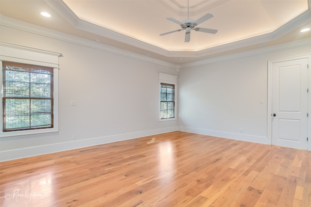 empty room with a raised ceiling, crown molding, and light hardwood / wood-style floors