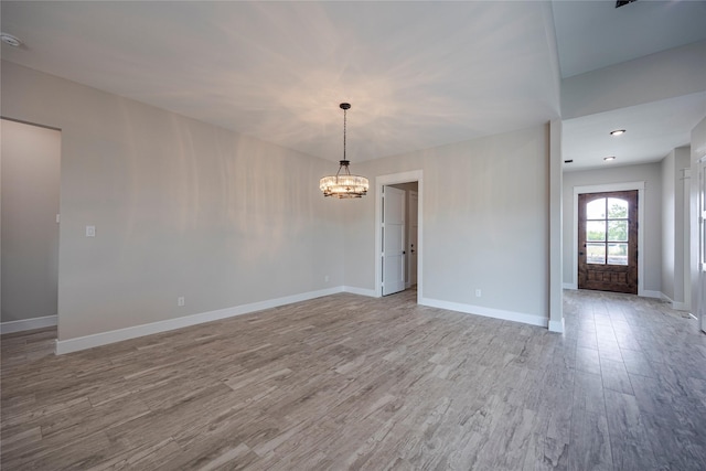 empty room featuring an inviting chandelier and light wood-type flooring