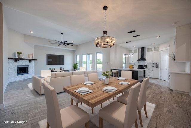 dining area with a fireplace, light hardwood / wood-style floors, and ceiling fan with notable chandelier