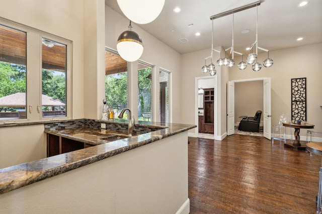 kitchen featuring pendant lighting, dark stone counters, dark hardwood / wood-style flooring, and sink