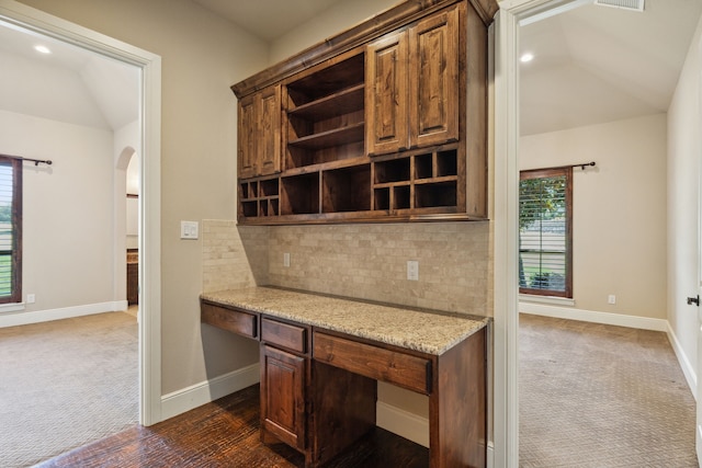 kitchen with tasteful backsplash, dark carpet, light stone countertops, and vaulted ceiling