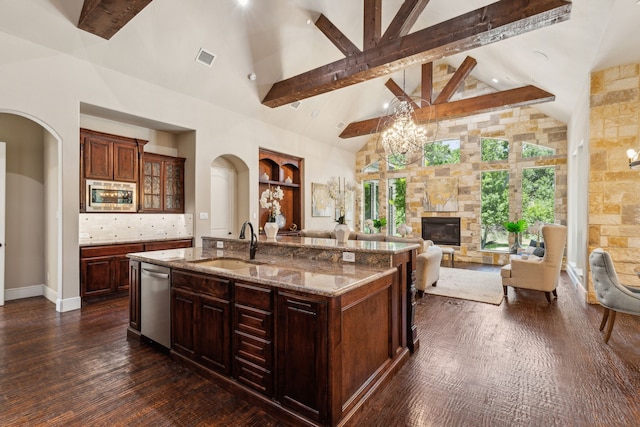 kitchen with a fireplace, an island with sink, sink, stainless steel appliances, and beam ceiling