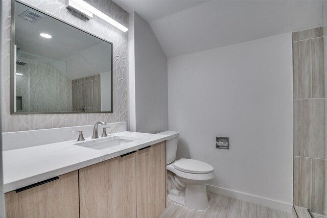 bathroom with vanity, vaulted ceiling, toilet, tiled shower, and wood-type flooring