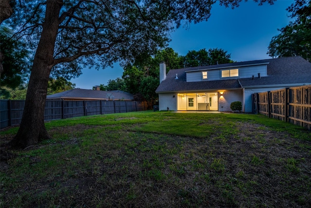 back house at dusk featuring a lawn