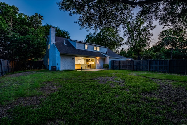 back house at dusk featuring a lawn, cooling unit, and a patio area