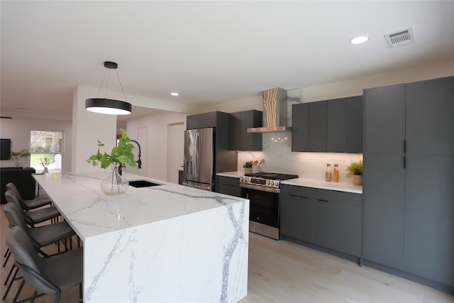 kitchen with appliances with stainless steel finishes, light wood-type flooring, backsplash, wall chimney exhaust hood, and pendant lighting