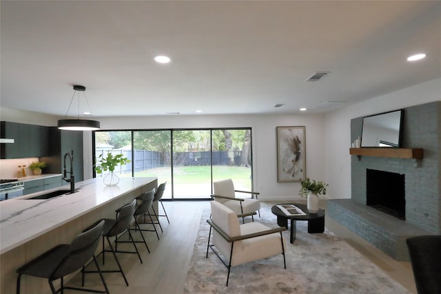 living room with a brick fireplace, sink, and light wood-type flooring