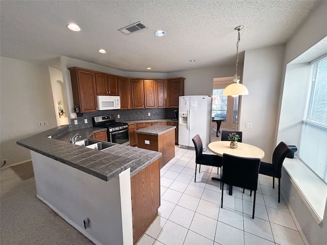 kitchen with hanging light fixtures, white appliances, kitchen peninsula, light tile patterned floors, and sink