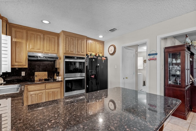 kitchen featuring dark stone countertops, light tile patterned floors, black fridge, stainless steel double oven, and sink