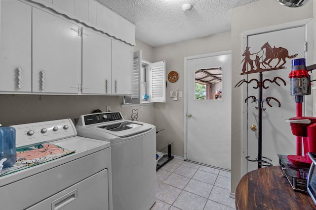 laundry room featuring cabinets, washer and clothes dryer, a textured ceiling, and light tile patterned floors