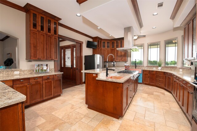 kitchen with high quality fridge, island range hood, a center island with sink, light stone counters, and light tile floors