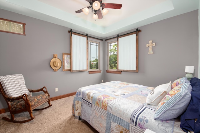 carpeted bedroom with a barn door, ceiling fan, and a raised ceiling