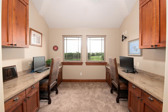 carpeted home office with built in desk and lofted ceiling