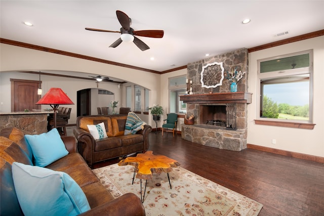 living room with a stone fireplace, crown molding, wood-type flooring, and ceiling fan