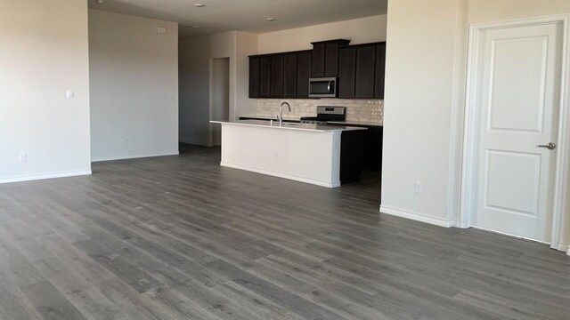 kitchen with dark hardwood / wood-style flooring, backsplash, appliances with stainless steel finishes, a kitchen island with sink, and sink