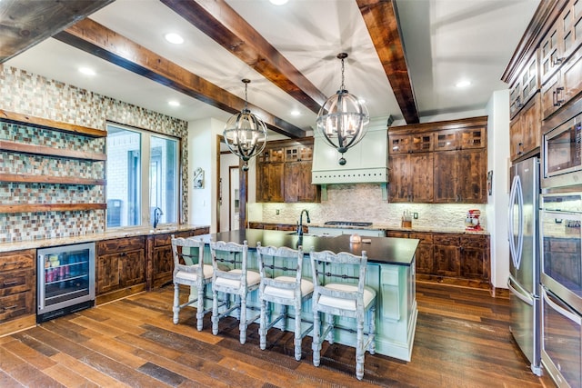 kitchen featuring an inviting chandelier, wine cooler, decorative light fixtures, a center island with sink, and appliances with stainless steel finishes