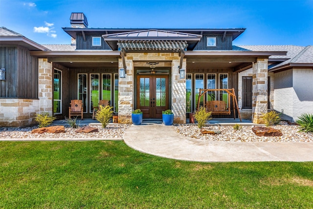 entrance to property featuring french doors, a porch, and a lawn