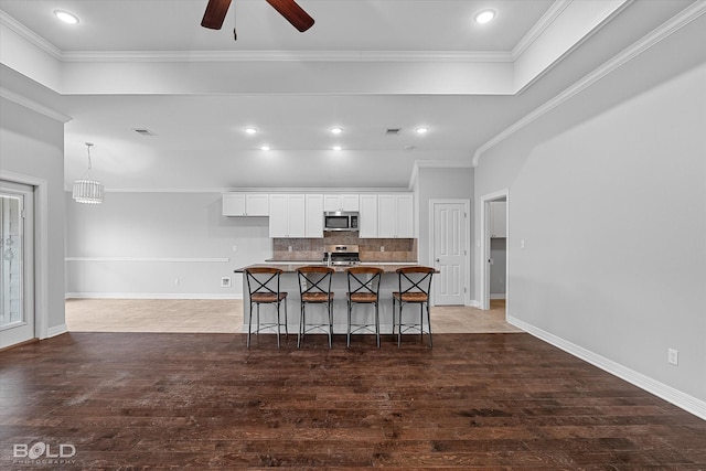 kitchen featuring a kitchen bar, white cabinetry, tasteful backsplash, appliances with stainless steel finishes, and a kitchen island with sink