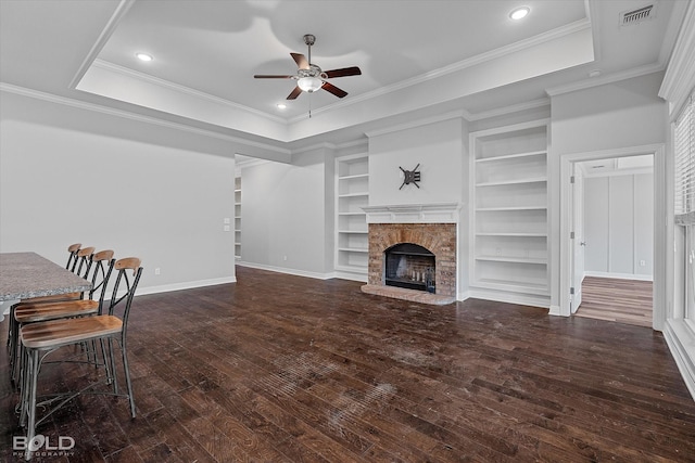 living room with a brick fireplace, ornamental molding, dark hardwood / wood-style flooring, a raised ceiling, and ceiling fan