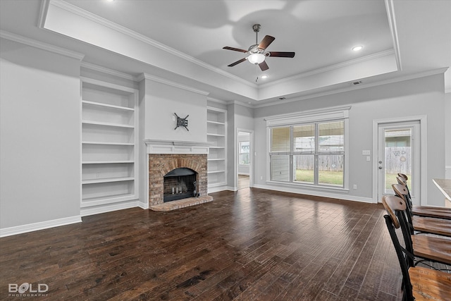 unfurnished living room featuring crown molding, a brick fireplace, a tray ceiling, and dark wood-type flooring