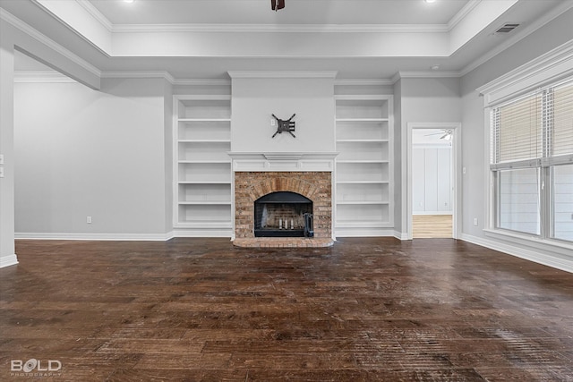 unfurnished living room featuring built in shelves, a tray ceiling, a fireplace, and dark hardwood / wood-style flooring