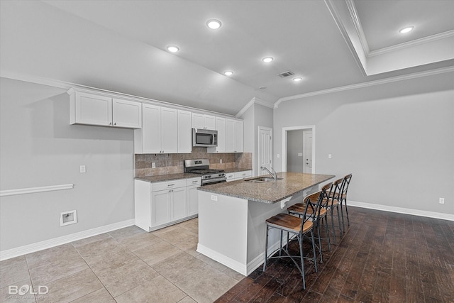 kitchen featuring appliances with stainless steel finishes, white cabinetry, sink, a kitchen bar, and a center island with sink