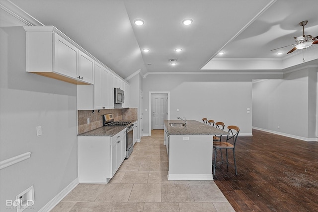 kitchen featuring appliances with stainless steel finishes, white cabinetry, sink, dark stone countertops, and a kitchen breakfast bar