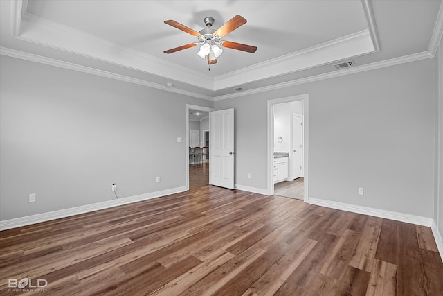 unfurnished bedroom featuring crown molding, wood-type flooring, a tray ceiling, and ensuite bathroom