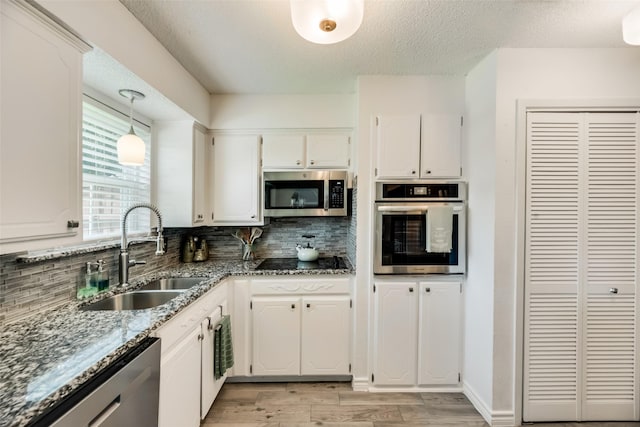 kitchen featuring appliances with stainless steel finishes, pendant lighting, sink, white cabinets, and decorative backsplash