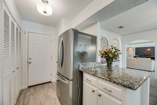 kitchen featuring dark stone countertops, stainless steel refrigerator, white cabinets, and light wood-type flooring