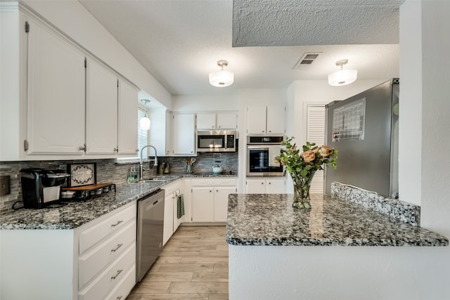 kitchen with appliances with stainless steel finishes, backsplash, dark stone counters, sink, and white cabinetry