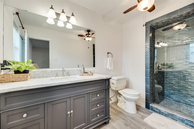 bathroom with ceiling fan, hardwood / wood-style floors, tiled shower, vanity, and toilet