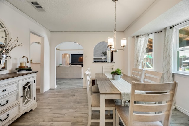 dining space with an inviting chandelier, crown molding, a textured ceiling, and light wood-type flooring