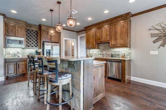 kitchen featuring ornamental molding, hanging light fixtures, light stone countertops, a kitchen island, and appliances with stainless steel finishes