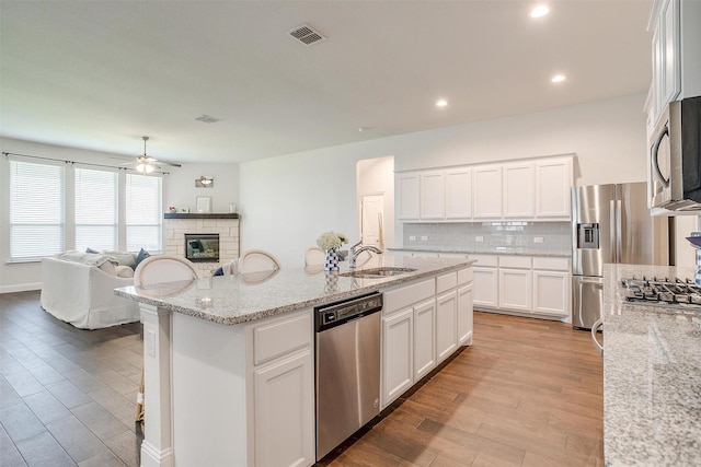 kitchen with sink, appliances with stainless steel finishes, light stone counters, white cabinets, and a center island with sink