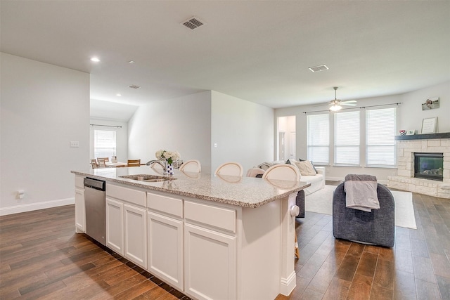 kitchen featuring sink, dishwasher, white cabinets, a center island with sink, and a stone fireplace