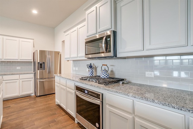 kitchen featuring tasteful backsplash, appliances with stainless steel finishes, light stone countertops, light hardwood / wood-style floors, and white cabinets