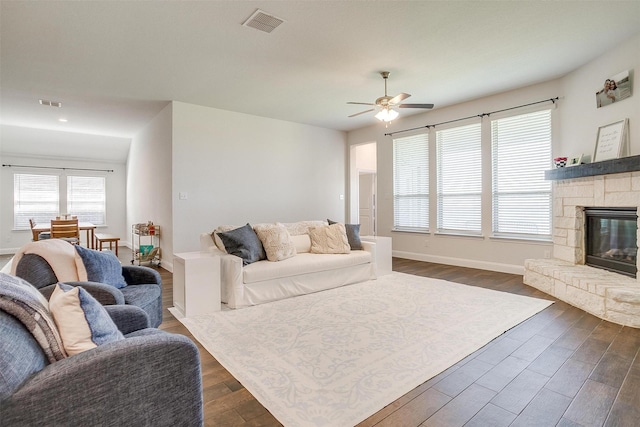 living room featuring dark hardwood / wood-style flooring, a stone fireplace, and ceiling fan