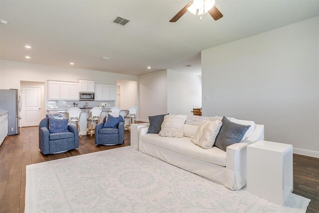 living room featuring a stone fireplace, ceiling fan, and dark wood-type flooring