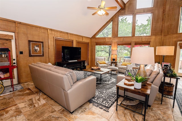 tiled living room featuring high vaulted ceiling, wood walls, and ceiling fan