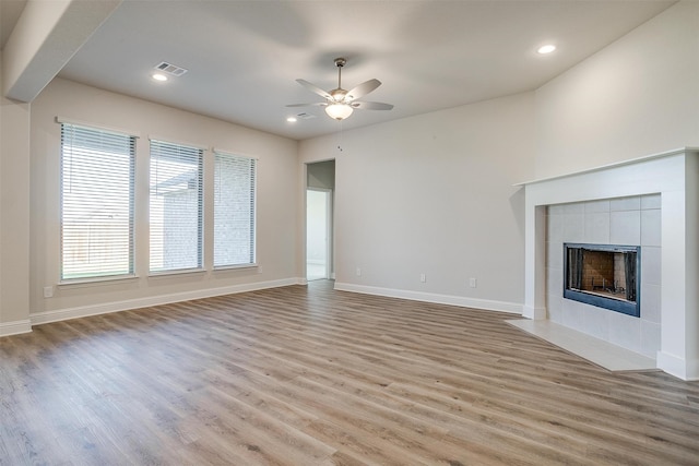 unfurnished living room featuring ceiling fan, light wood-type flooring, and a tiled fireplace